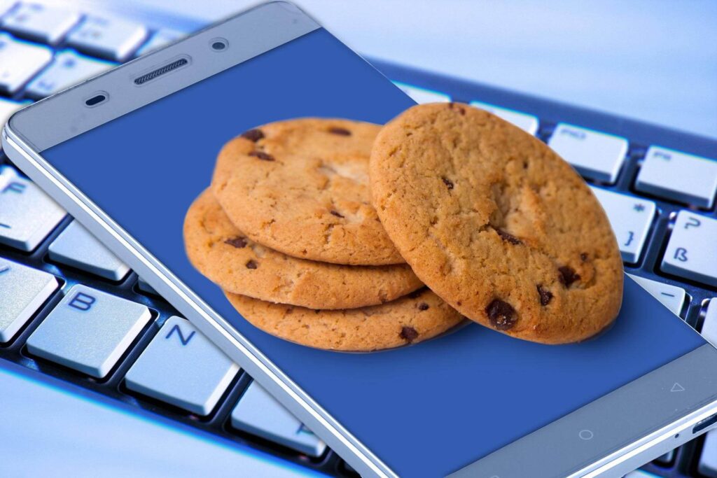 Three cookies lying on a cell phone next to a keyboard